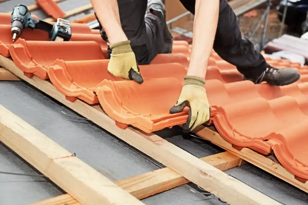 Pose de tuiles en terre cuite par un couvreur sur une charpente, pour une couverture durable et esthétique.