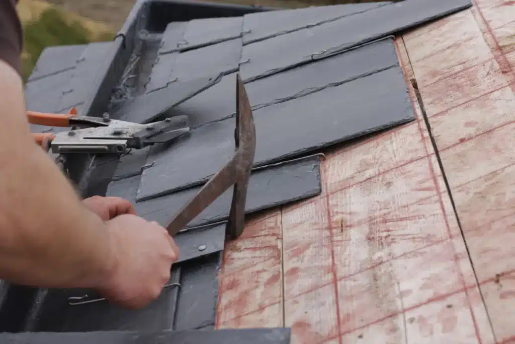 Installation de tuiles d'ardoise sur une toiture en rénovation, assurant résistance et isolation. ​​