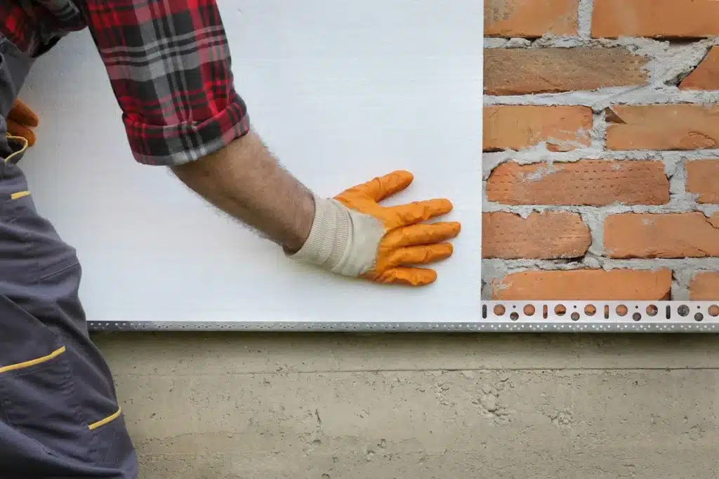 Pose d'un panneau isolant sur une façade extérieure en briques pour une meilleure isolation thermique des murs.