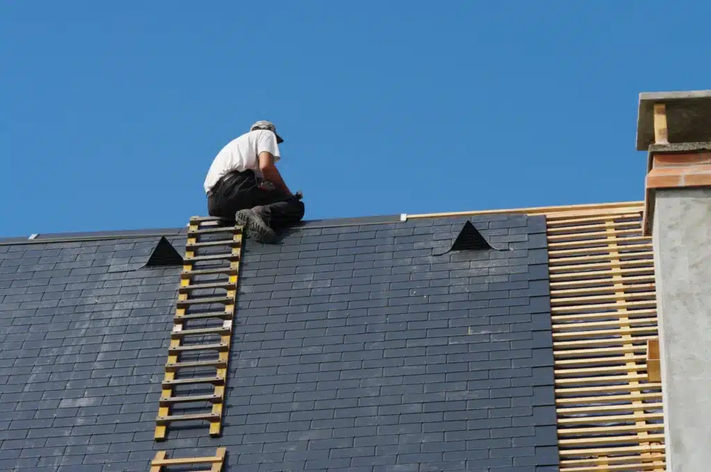 Couvreur travaillant en hauteur sur la pose d'ardoises, utilisant une échelle spécialisée pour atteindre le sommet du toit. ​​